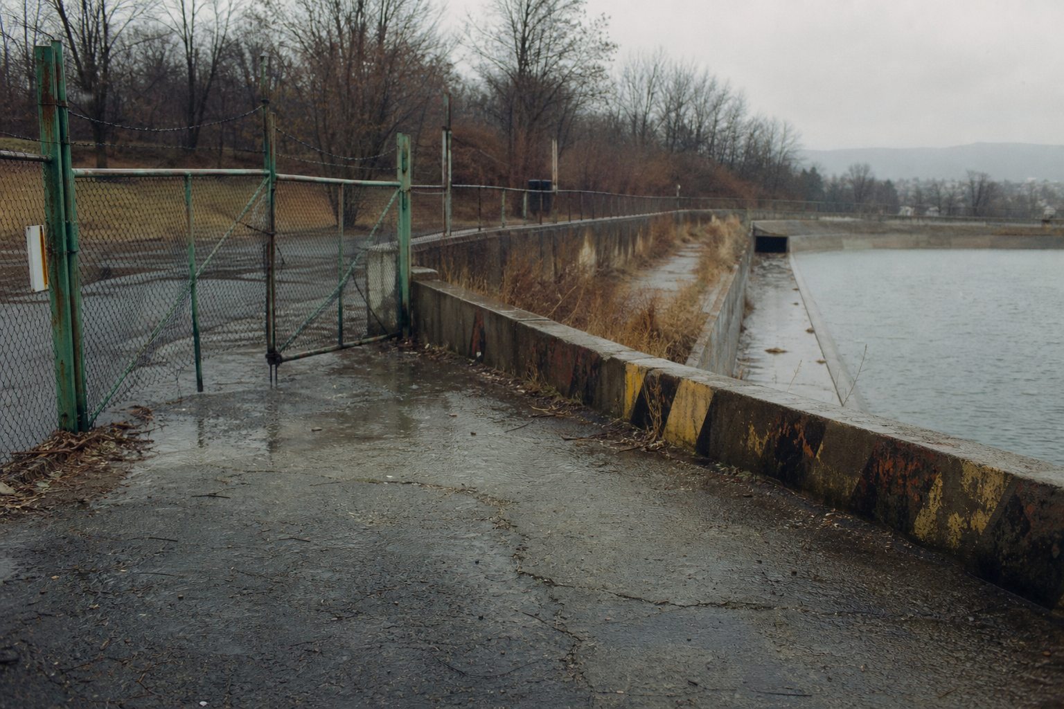 A maintenance gate beside a rain-darkened reservoir spillway